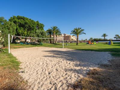 Sandvolleyballfeld mit Netz auf einer grünen Hotelwiese unter blauem Himmel.