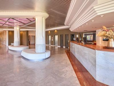 Großer Hotellobby-Bereich mit Marmorboden, Säulen und Rezeptionstresen mit Blumen.