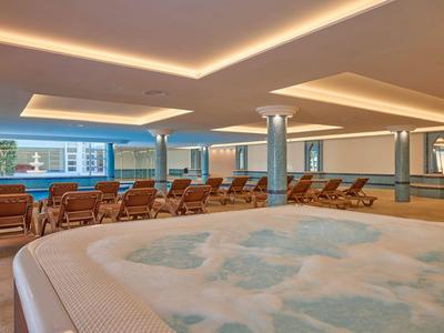 Innenbereich eines Hotels mit whirlpool und mehreren Liegestühlen vor bodentiefen Fenstern.