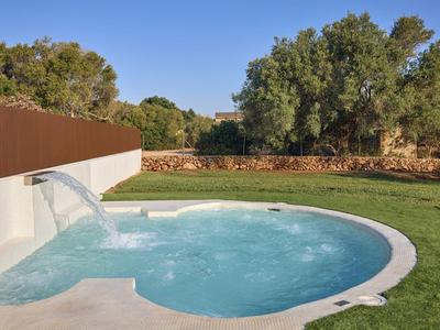 Runder Pool mit Wasserfall umgeben von grüner Wiese und Bäumen im Hotelgarten.