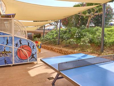 Blauer Tischtennistisch unter Sonnensegeln neben Basketballkorb im Außenbereich.