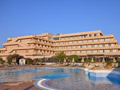 Hotel mit mehreren Etagen und großem Pool vor blauem Himmel.