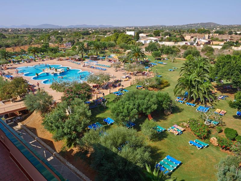 Grande piscina all'aperto con lettini e area giardino in un complesso alberghiero sotto un cielo sereno.
