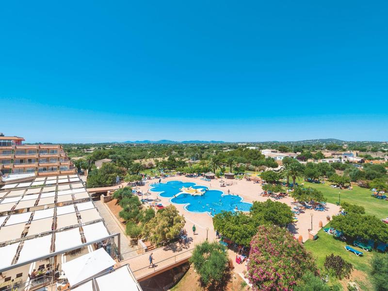 Vista grandangolare di una grande piscina all'aperto con lettini in un complesso alberghiero sotto un cielo sereno.