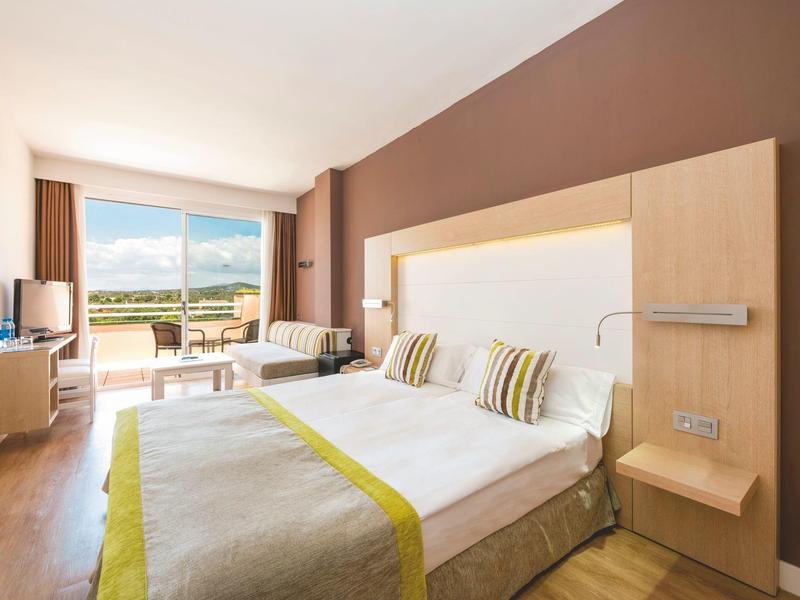 Camera d'hotel luminosa con letto matrimoniale, decorazione moderna e balcone con vista sulle montagne.