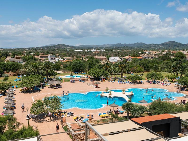 Grande piscina all'aperto in un resort con sedie a sdraio e alberi sotto un cielo azzurro.