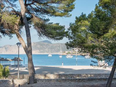 Výhled na zátoku s plachetnicemi, obklopenou stromy a kamennou plochou v popředí.