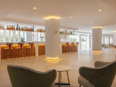 Světlá hotelová barová zóna s barovými židlemi, pultem a pohodlnými křesly v popředí