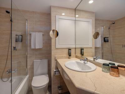 Moderní koupelna se umyvadlem, zrcadlem, toaletou a vanou s sprchovým koutem.