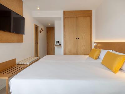 Moderní hotelový pokoj s velkou postelí, žlutými polštáři, televizí a dřevěným nábytkem.