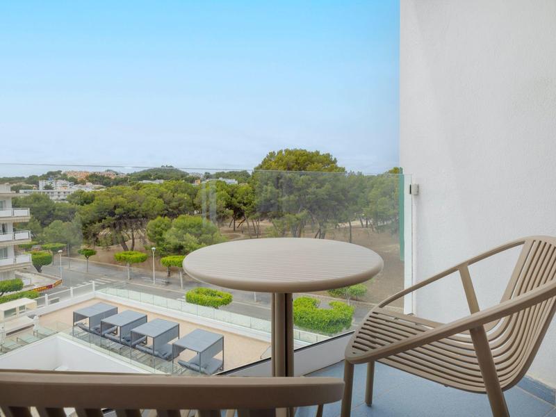 Balkon s kulatým stolem a židlí s výhledem na bazén a zelenou krajinu.