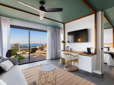 Camera d'hotel moderna con zona salotto, TV e vista sulla terrazza e sul mare.