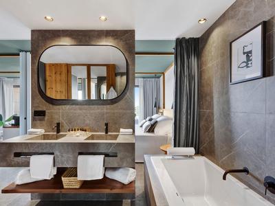 Bagno moderno con doppi lavandini, grande specchio rotondo e vasca da bagno accanto a pareti grigie.