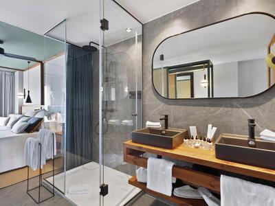 Camera d'hotel moderna con bagno aperto, doccia in vetro e doppio lavabo di design.