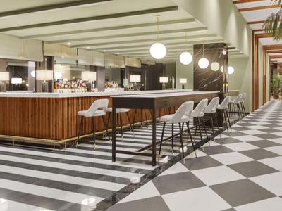 Area bar dell'hotel moderna con bancone in legno, sgabelli bianchi e pavimento a scacchi bianco e nero.