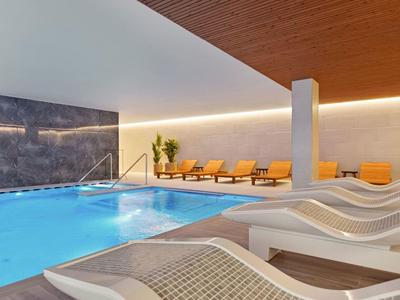 Piscina interna moderna con sdraio e decorazioni in legno caldo in un hotel.