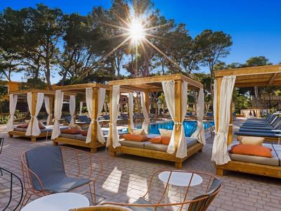 Lussuosa lounge esterna con lettini e tende da sole sotto gli alberi in una giornata di cielo sereno.