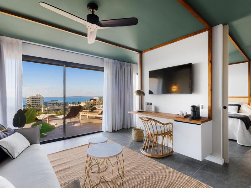 Camera d'hotel moderna con zona salotto, TV e vista sulla terrazza e sul mare.