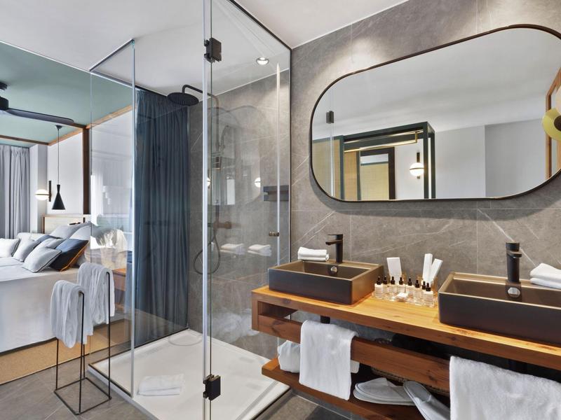 Camera d'hotel moderna con bagno aperto, doccia in vetro e doppio lavabo di design.