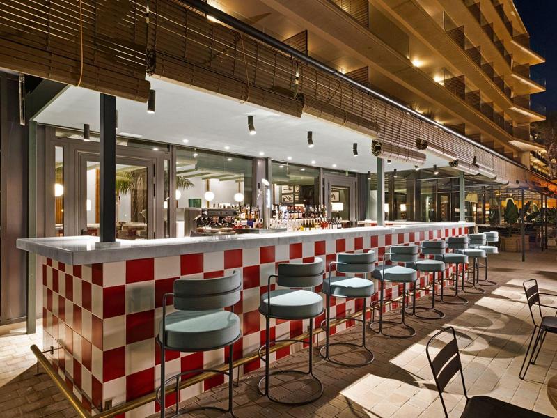 Moderna area bar esterna con bancone a scacchi rossi e bianchi e sgabelli imbottiti blu.