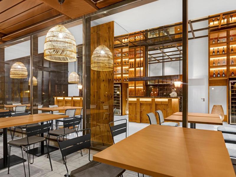 Ristorante moderno con soffitto in legno, illuminazione calda e tavoli e sedie accoglienti.