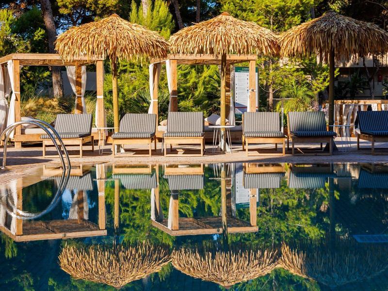 Sedie a sdraio e padiglioni con tetto di paglia vicino alla piscina di un resort al tramonto.
