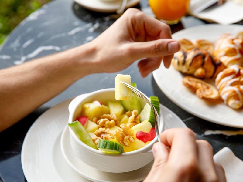 Persona che mangia un'insalata di frutta fresca con cornetti a un tavolo.