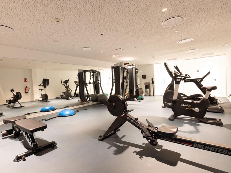 Palestra luminosa con varie attrezzature per allenamento e panche per pesi.