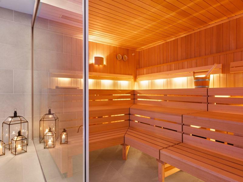 Area sauna con pannelli di legno chiaro, panche e lanterne decorative sul pavimento.