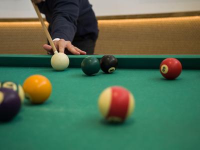 Osoba hrající kulečník u zeleného stolu s několika barevnými koulemi.