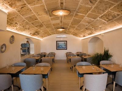 Interno di un ristorante con tavoli in legno, sedie grigie e soffitto a volta in pietra.