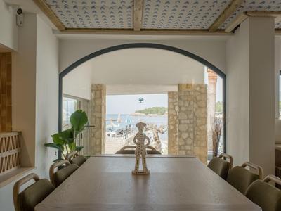 Area pranzo interna con vista sulla terrazza e sul mare attraverso un arco.