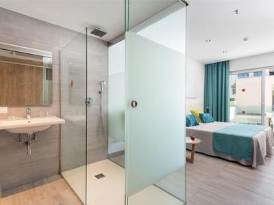 Camera d'hotel moderna con bagno aperto e letto matrimoniale, separati da parete in vetro.