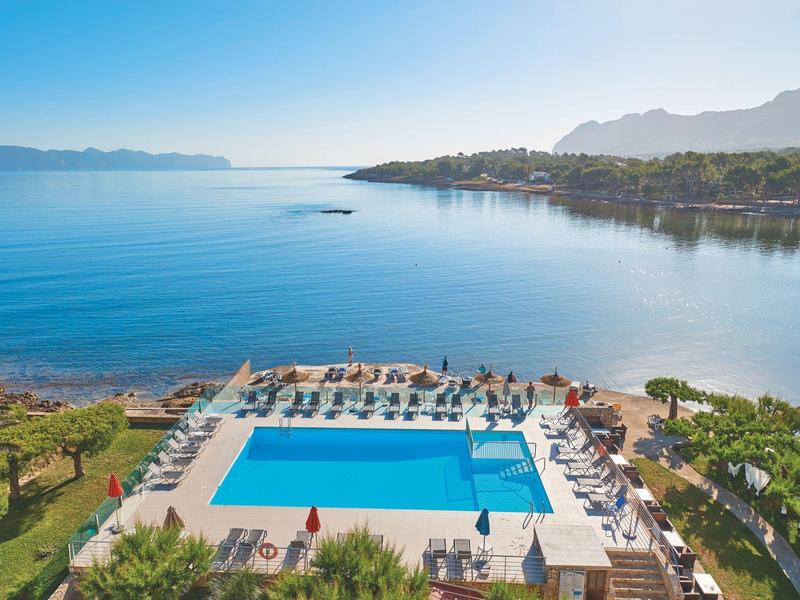 Una grande piscina all'aperto con lettini, circondata da paesaggio verde e vista sul mare blu calmo.