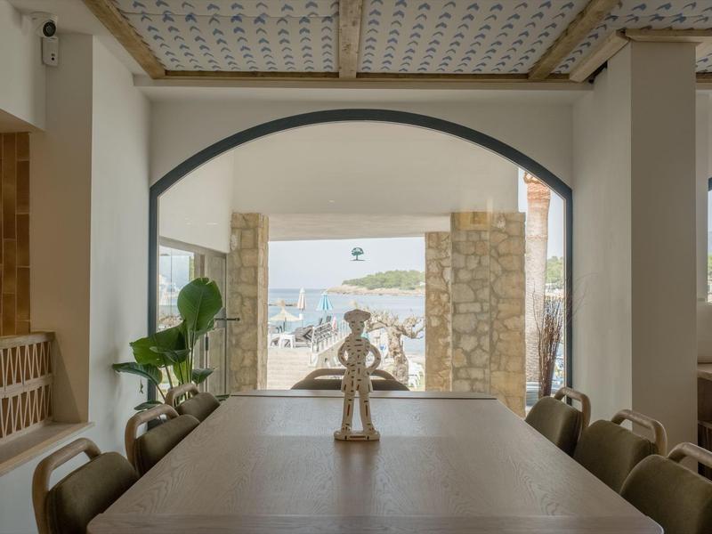 Area pranzo interna con vista sulla terrazza e sul mare attraverso un arco.