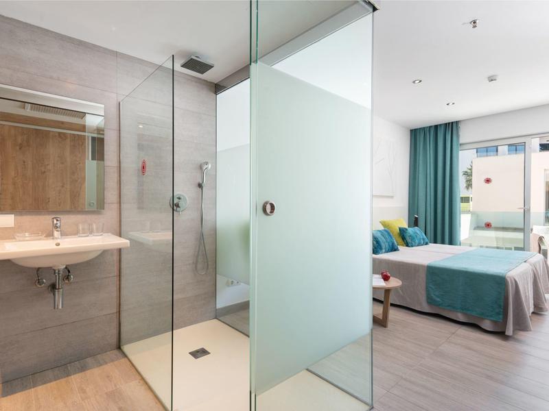 Camera d'hotel moderna con bagno aperto e letto matrimoniale, separati da parete in vetro.