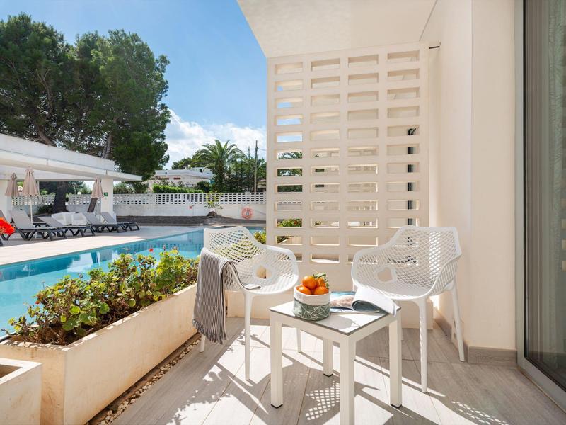 Un balcone con tavolo e sedie, un asciugamano e vista su una piscina e lettini.