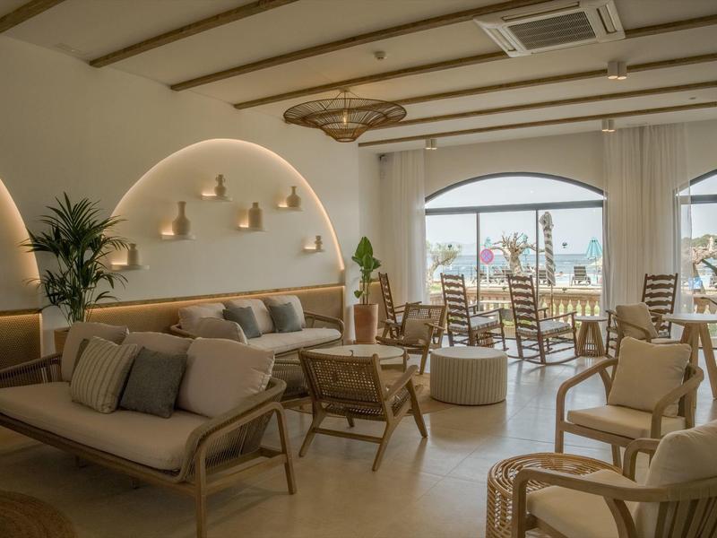 Zona lounge accogliente con mobili in legno e rattan, grandi finestre e vista sul porto.