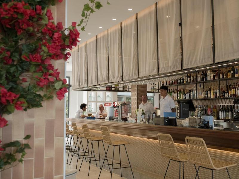 Area bar in hotel con sgabelli alti e fiori rossi sulla parete.