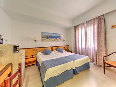 Bright hotel room with two single beds, nightstands, and a window with curtains.