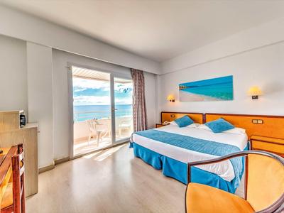 Habitación de hotel luminosa con cama doble, puerta al balcón y vista al mar.