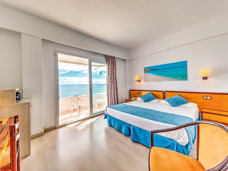 Bright hotel room with double bed, sea view through large windows, and modern furnishings.