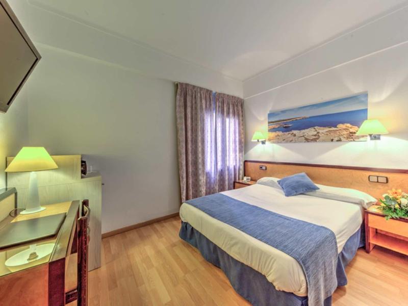 Cozy hotel room with double bed, wooden floor, desk, and decorative picture above the bed.