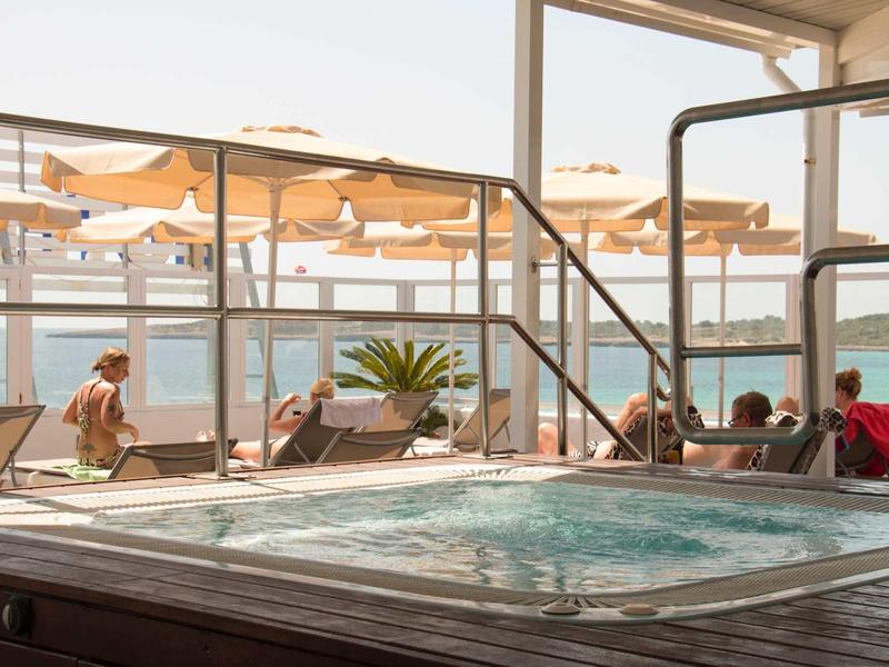 Indoor hot tub overlooking terrace and sea with sun umbrellas.