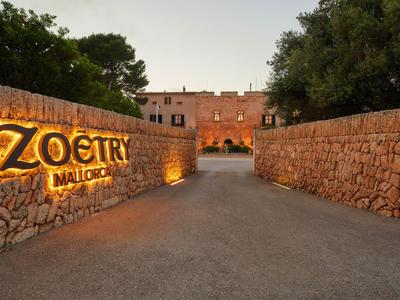 Des murs en pierre encadrent l'entrée du Zoetry Mallorca Resort au crépuscule.