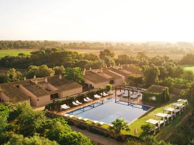 Rezort s velkým venkovním bazénem, lehátky a obklopený zelení při západu slunce.