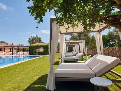 Lehátka pod zastíněnými baldachýny vedle modrého bazénu s zeleným trávníkem.