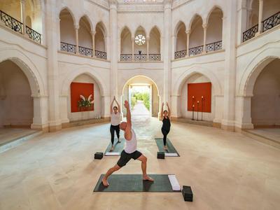 Tři ženy cvičí jógu v jasném, elegantním interiéru s oblouky a vysokým stropem.