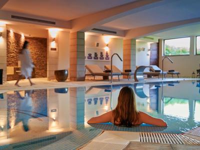 Vnitřní bazén s lehátky, teplým osvětlením a velkými okny s výhledem na zeleň.