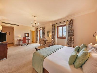 Prostorný hotelový pokoj s velkou postelí, posezením, pracovním stolem a elegantním zařízením.